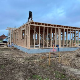 TKB Szymon Pukownik - Konstrukcja domu szkieletowego w trakcie budowy we Wrocławiu. Widoczny szkielet ścian i stropu, fundament oraz pracownik na dachu. Kontrola kierownika budowy.