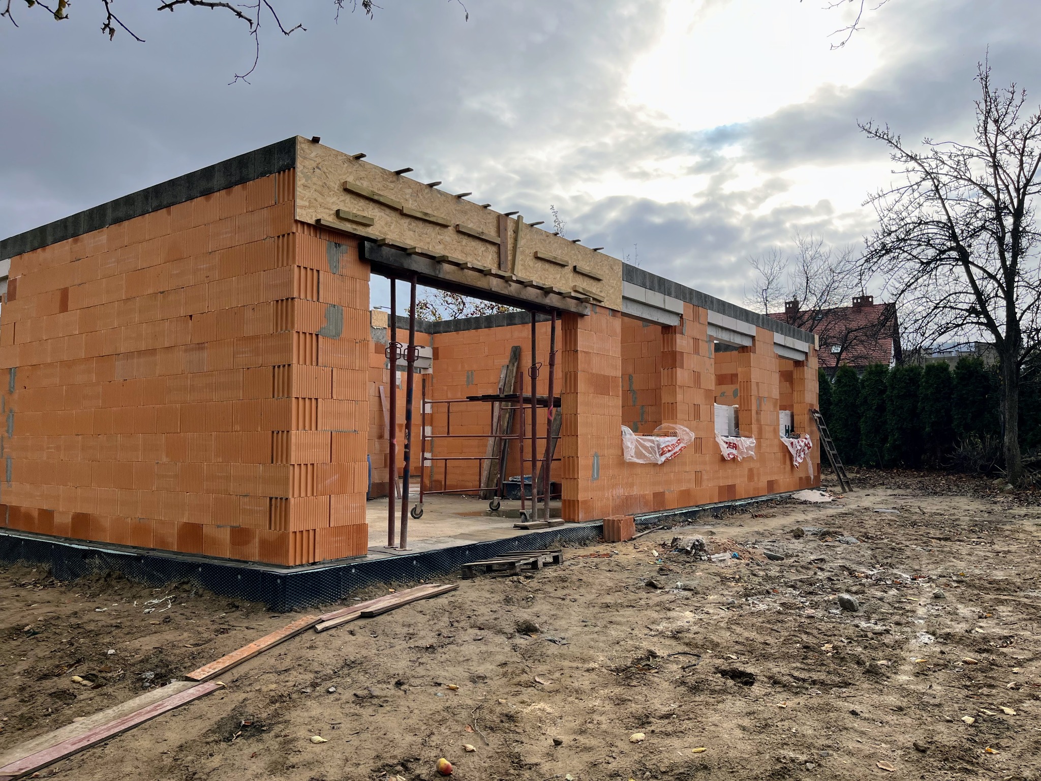 Budowa domu jednorodzinnego w trakcie wznoszenia ścian z pustaków ceramicznych. Widoczne rusztowania i elementy konstrukcyjne nadproży.