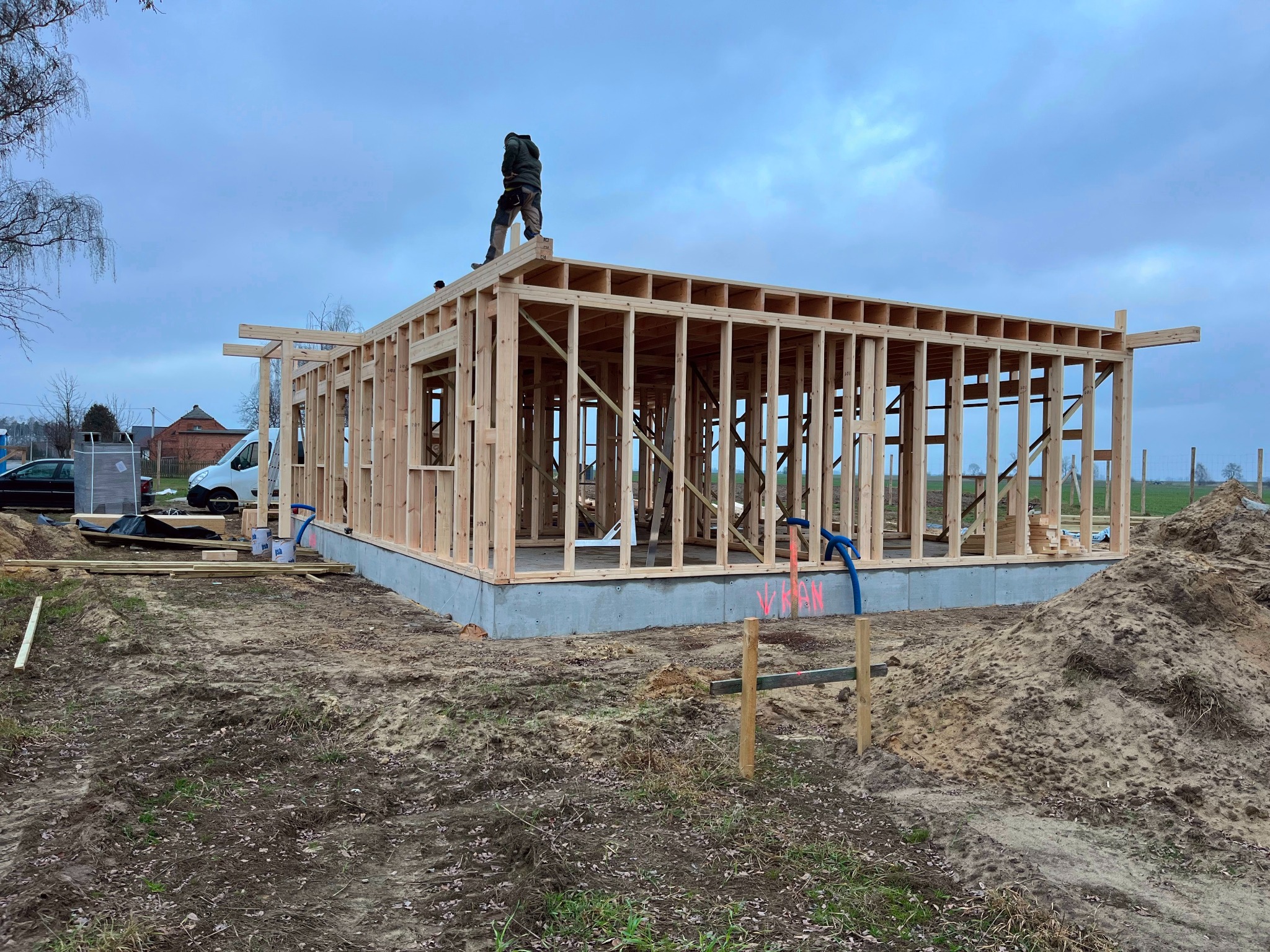 Konstrukcja domu szkieletowego w trakcie budowy we Wrocławiu. Widoczny szkielet ścian i stropu, fundament oraz pracownik na dachu. Kontrola kierownika budowy.