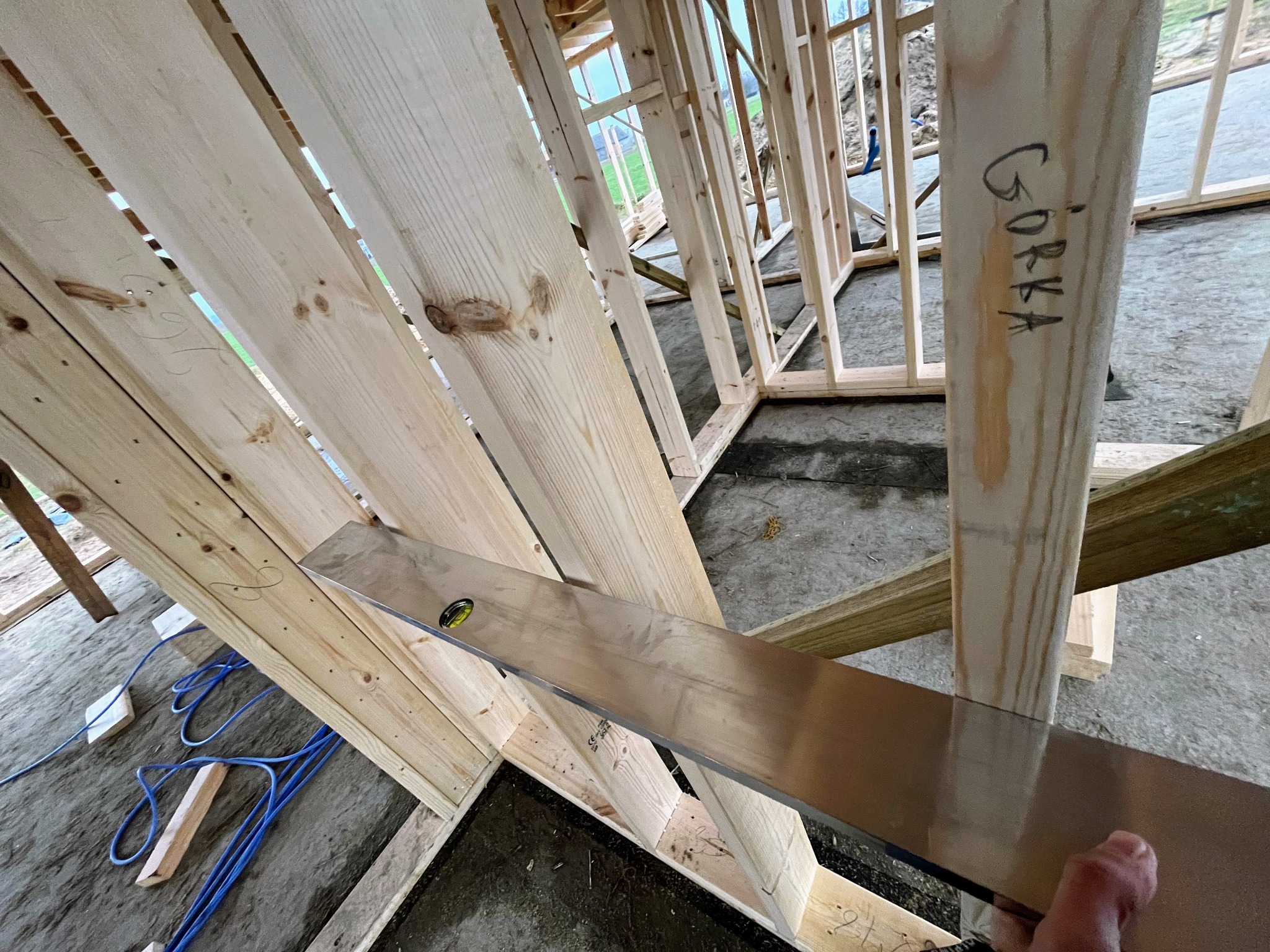 Sprawdzanie poziomu ściany szkieletowej domu jednorodzinnego za pomocą poziomicy. Widoczny słupek z napisem 'Górka' wskazujący na usterkę.