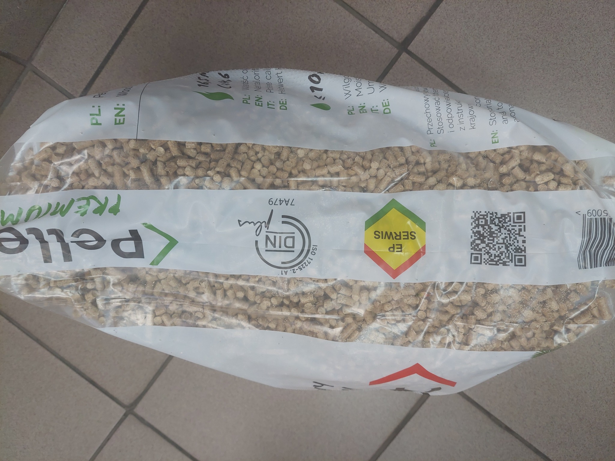 Worek z pelletem drzewnym premium, widoczne certyfikaty DINplus i EP Serwis, etykieta z informacjami o wartości opałowej i wilgotności, położony na podłodze z płytek.
