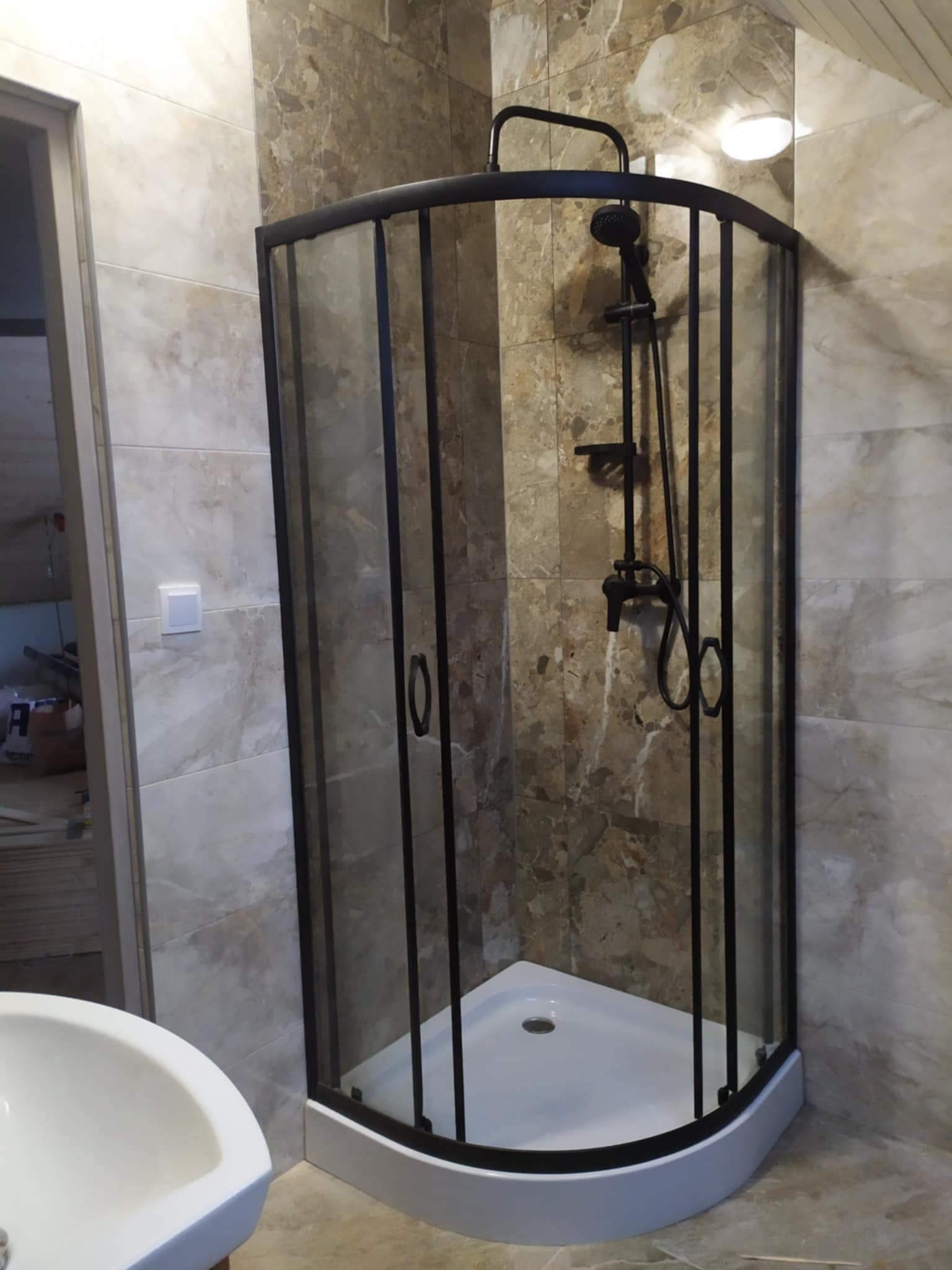 Narożna kabina prysznicowa z czarną ramą i armaturą na tle marmurowych płytek w łazience.