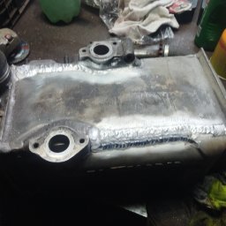 Jan-weld Usługi spawalnicze - Metalowy zbiornik po naprawie, widoczne ślady zajarzenia łuku i spoiny, w tle narzędzia warsztatowe i butla z gazem.