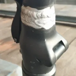 Szczegółowe zbliżenie na spaw na czarnej metalowej konstrukcji, prawdopodobnie ramy hulajnogi, z widoczną spoiną i elementami mocującymi.