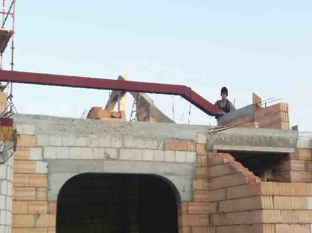 Wznoszenie konstrukcji z cegieł i betonu; widoczna stalowa belka stropowa i pracownik w odzieży roboczej na tle nieba.