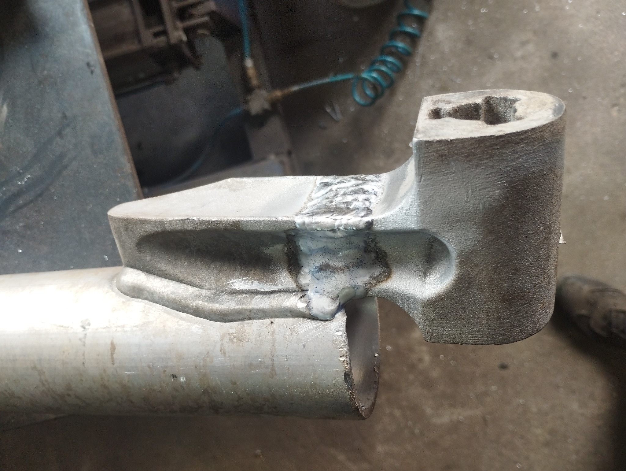 Szlifowany element metalowy z widocznym świeżym spawem łączącym rurę z grubszą częścią, widoczne ślady obróbki i niedoskonałości spoiny.