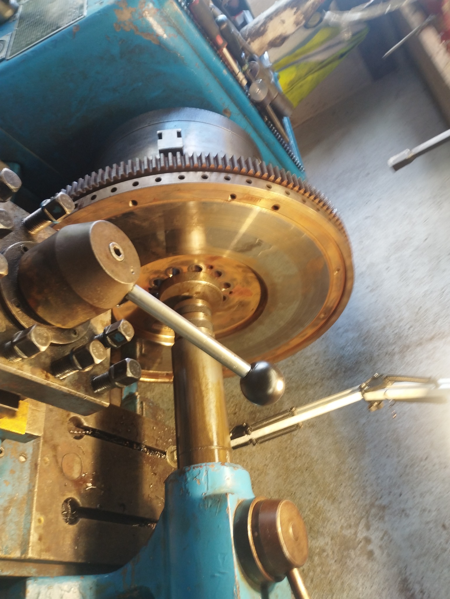 Detail metalowego koła z zębami, zamocowanego na maszynie z niebieską obudową, widoczne ślady użytkowania i narzędzia.