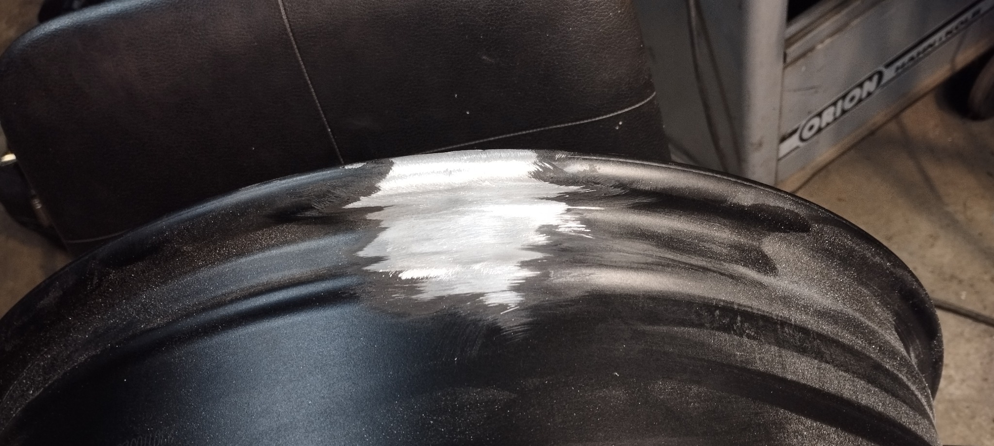 Fragment metalowego elementu, prawdopodobnie felgi samochodowej, z widocznymi śladami szlifowania i przygotowania do dalszej obróbki.