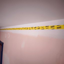 MULTI-FINISH - Przygotowanie do malowania: ściana pomalowana do połowy na różowo, górna część i sufit zabezpieczone żółtą taśmą malarską Washi Ultra Premium Painter's Tape.