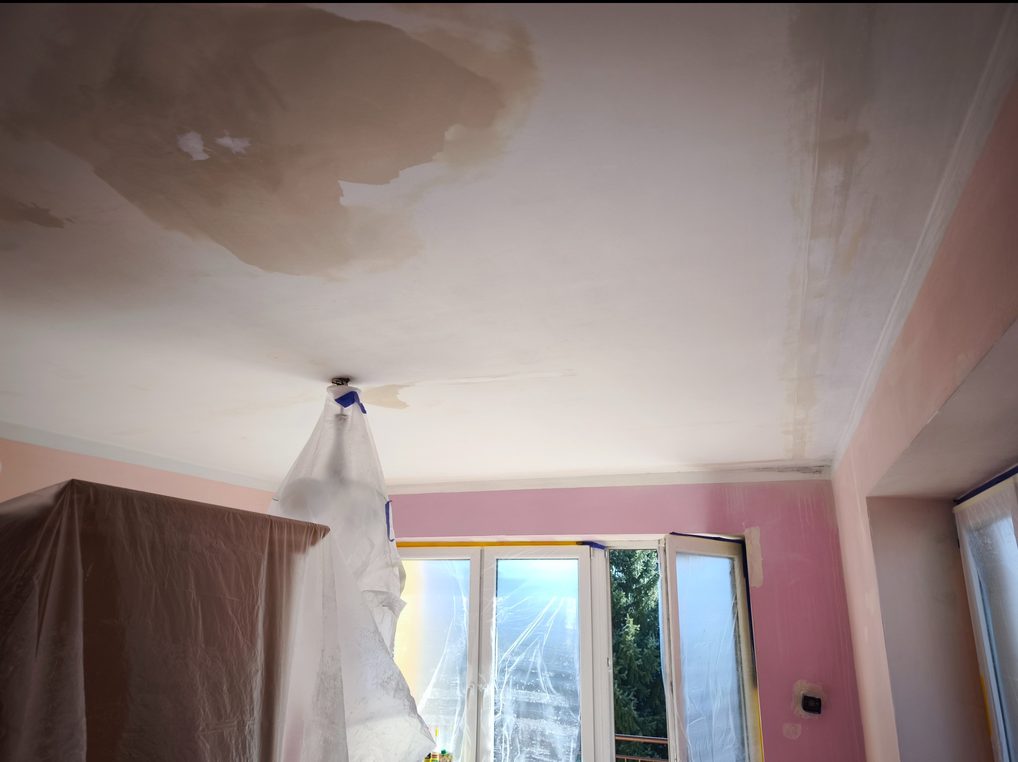 Przygotowania do malowania sufitu w Przyszowej: widoczne plamy po zalaniu, zabezpieczone folią meble i okna, ściany w różowym kolorze po szpachlowaniu.