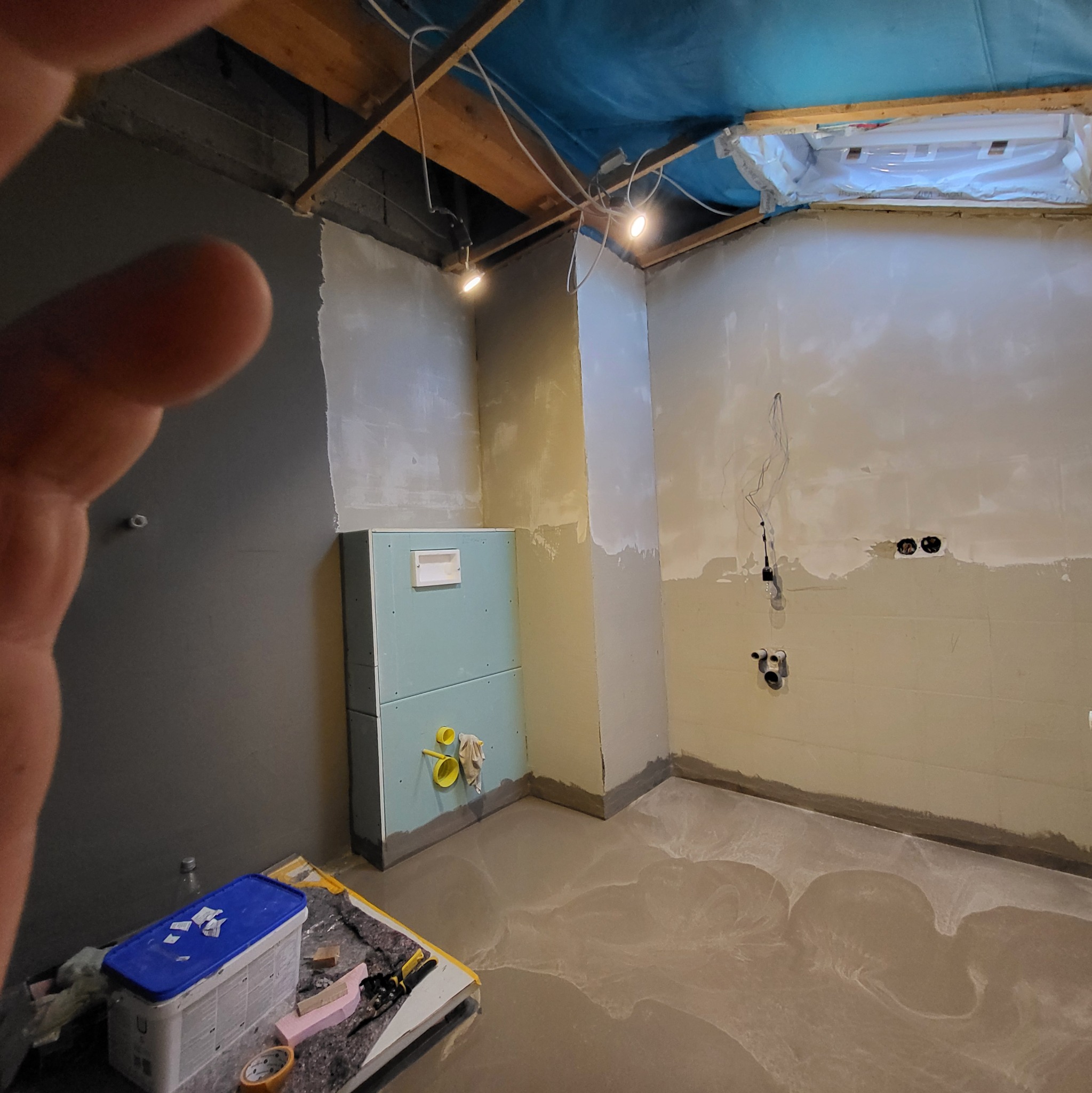 Wnętrze łazienki w trakcie remontu: zamontowany stelaż podtynkowy WC, wylewka na podłodze, ściany przygotowane do dalszych prac, widoczne przewody elektryczne i narzędzia.