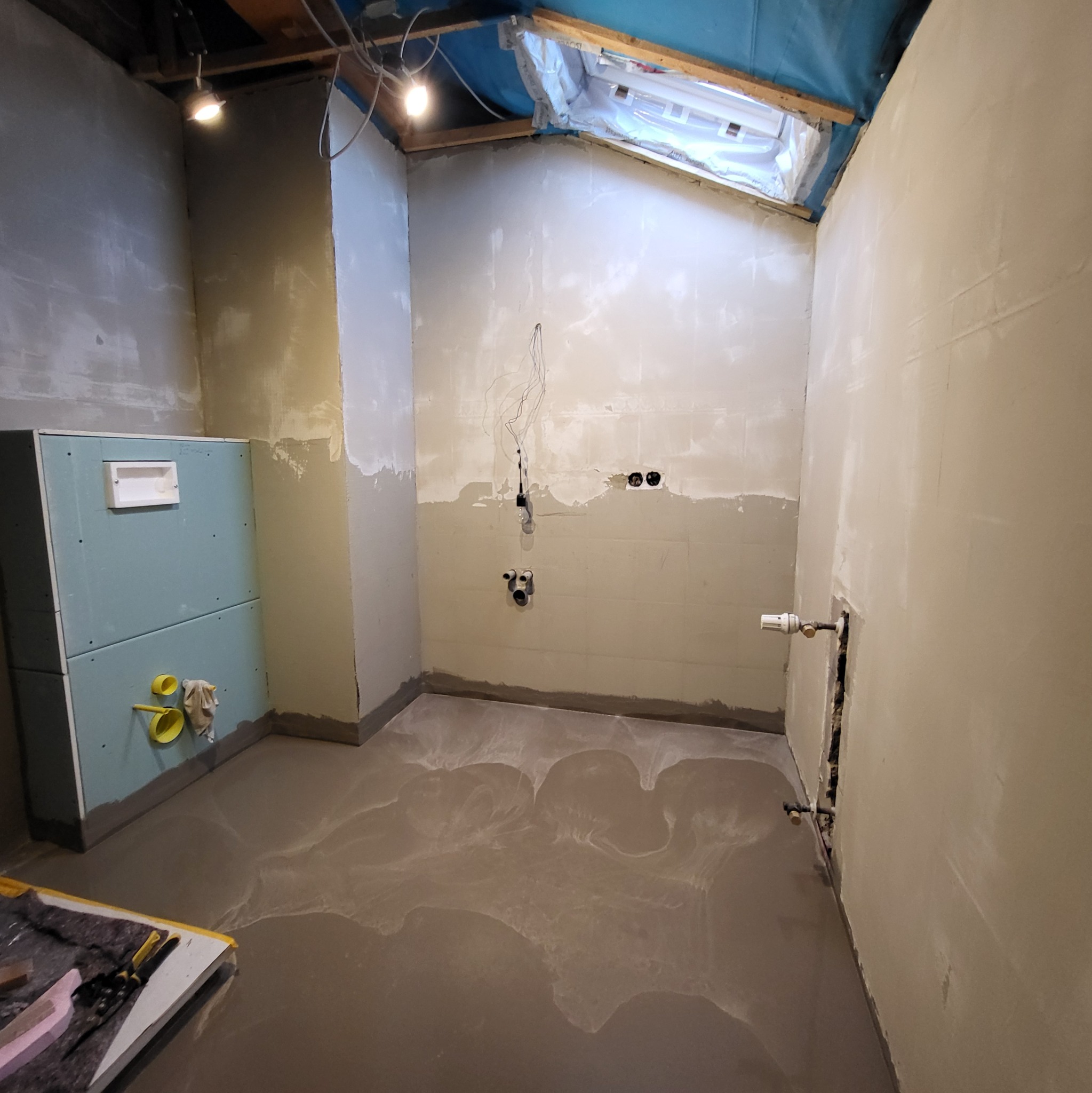 Surowy stan łazienki w trakcie prac wykończeniowych: wylewka podłogowa, częściowo osadzony stelaż WC z płyt gipsowo-kartonowych, przygotowane punkty instalacyjne, ściany po szpachlowaniu, widoczne...