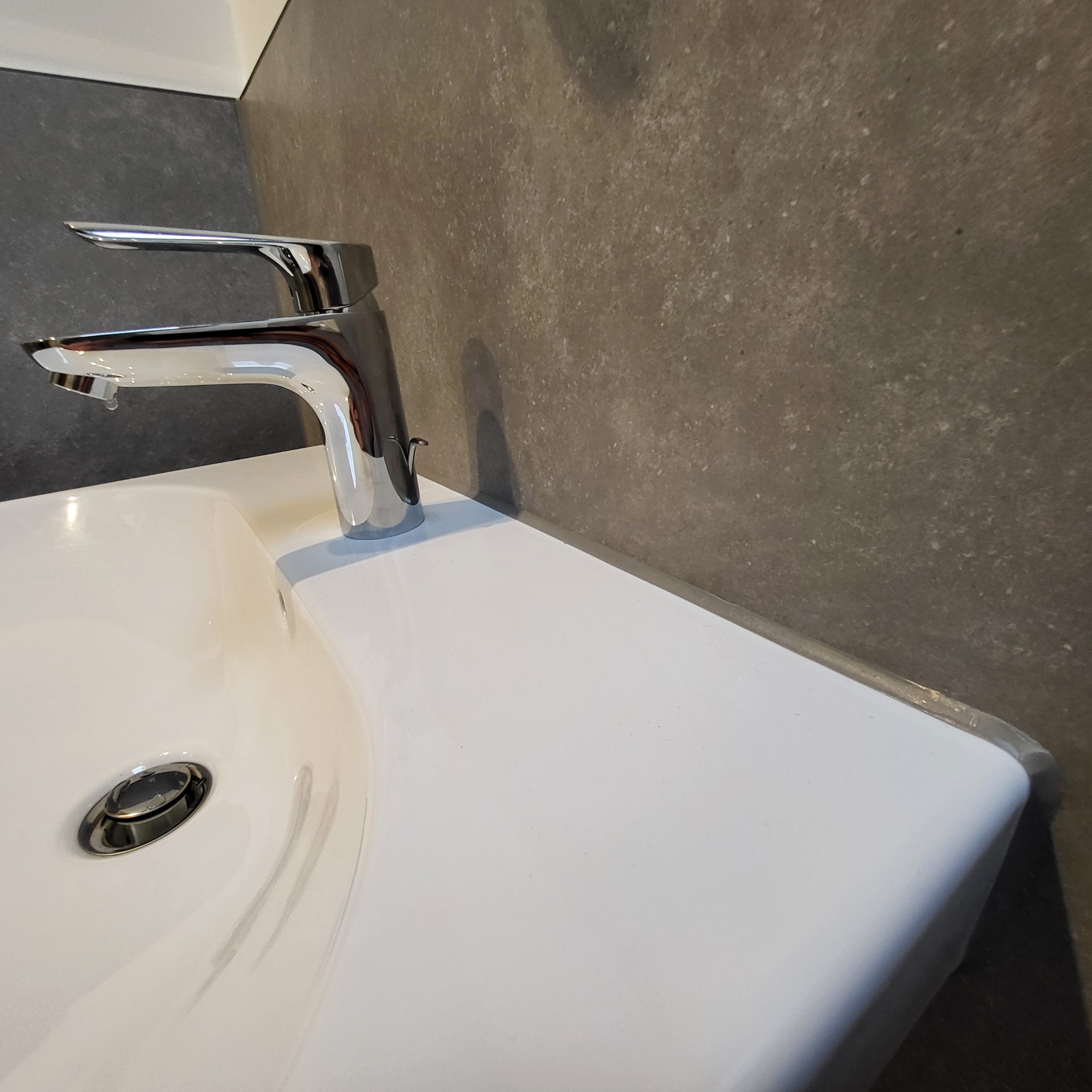 Bateria umywalkowa chromowana zamontowana na białej umywalce w łazience w Przyszowej, z szarą ścianą w tle.