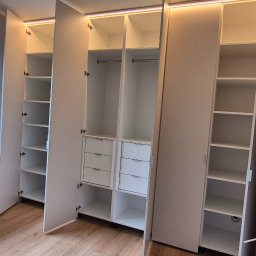 Verdini Andrzej Piotr - Jasna szafa wnękowa z oświetleniem LED, otwartymi półkami i szufladami, widoczna z boku okno z zielenią. Na podłodze skrzynka narzędziowa.