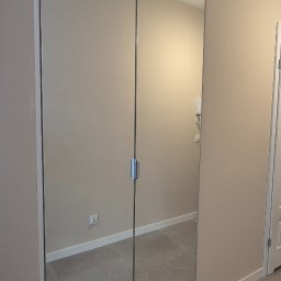 Verdini Andrzej Piotr - Nowoczesna szafa wnękowa z lustrzanymi drzwiami przesuwnymi, minimalistyczny design, szare płytki podłogowe, beżowe ściany, srebrne uchwyty.