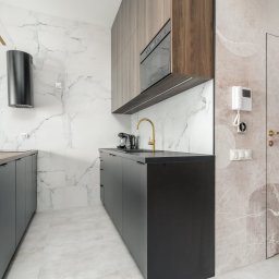 Verdini Andrzej Piotr - Nowoczesna kuchnia na wymiar w Szczecinie: czarne szafki, drewniane akcenty, marmurowe płytki i złota bateria, tworzą elegancką przestrzeń.