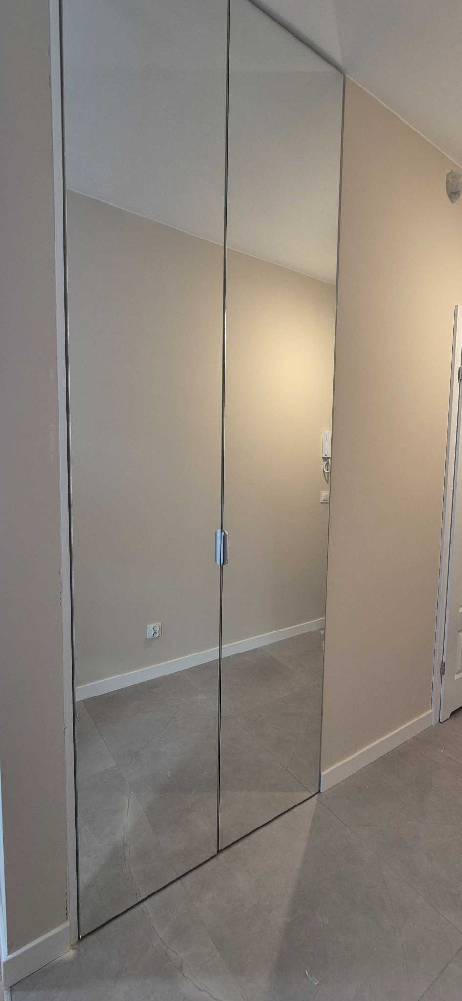 Nowoczesna szafa wnękowa z lustrzanymi drzwiami przesuwnymi, minimalistyczny design, szare płytki podłogowe, beżowe ściany, srebrne uchwyty.