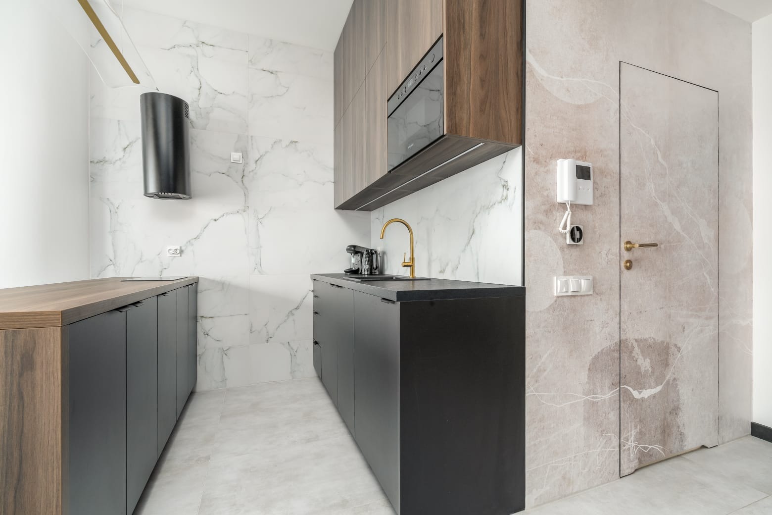 Nowoczesna kuchnia na wymiar w Szczecinie: czarne szafki, drewniane akcenty, marmurowe płytki i złota bateria, tworzą elegancką przestrzeń.