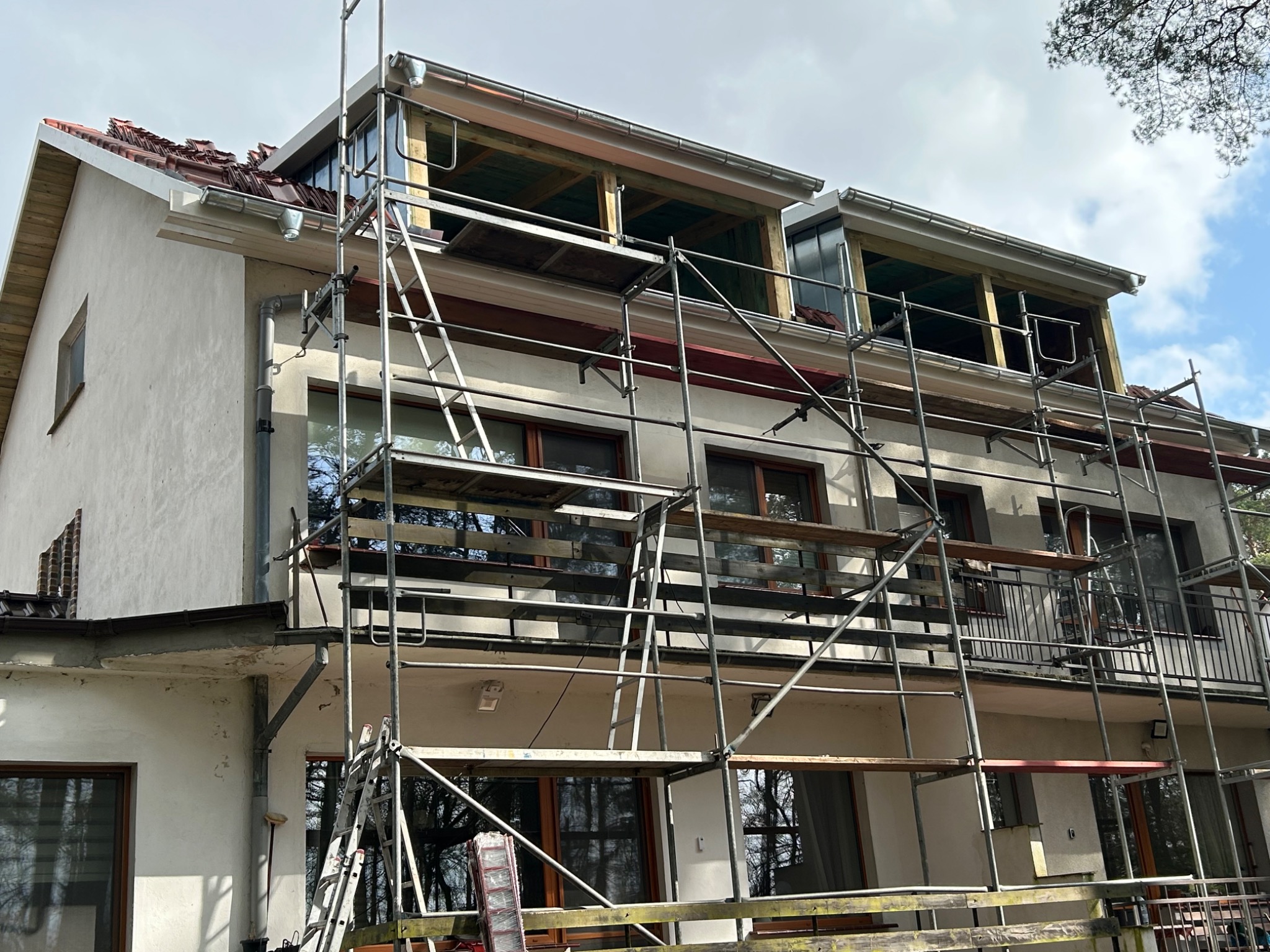 Dom w trakcie przebudowy z widocznymi rusztowaniami, częściowo zdjętym pokryciem dachu i konstrukcją drewnianą nowych okien dachowych.