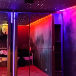 Adam Zygadło Abledo - Pokój z szafą przesuwną z lustrami, podświetlonymi krawędziami, fototapetą z motywem lasu i sufitem imitującym gwieździste niebo, oświetlony kolorowymi lampami LED.