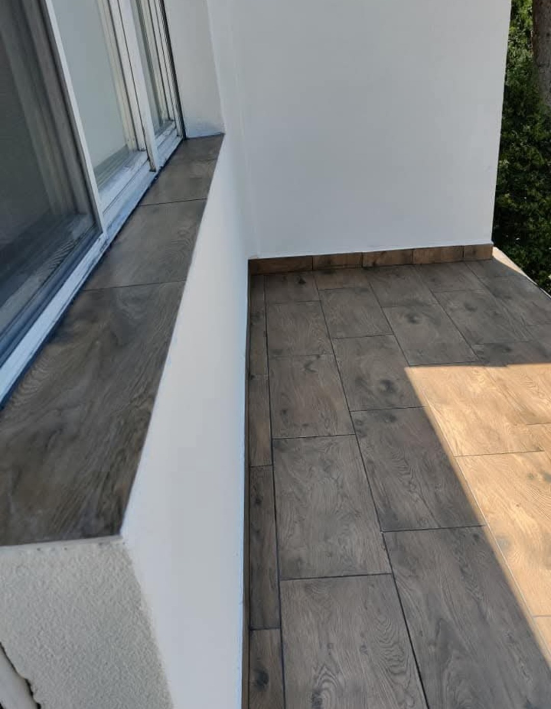 Wykończony balkon z płytkami imitującymi drewno na podłodze i parapecie okiennym, białe ściany, widok z góry.