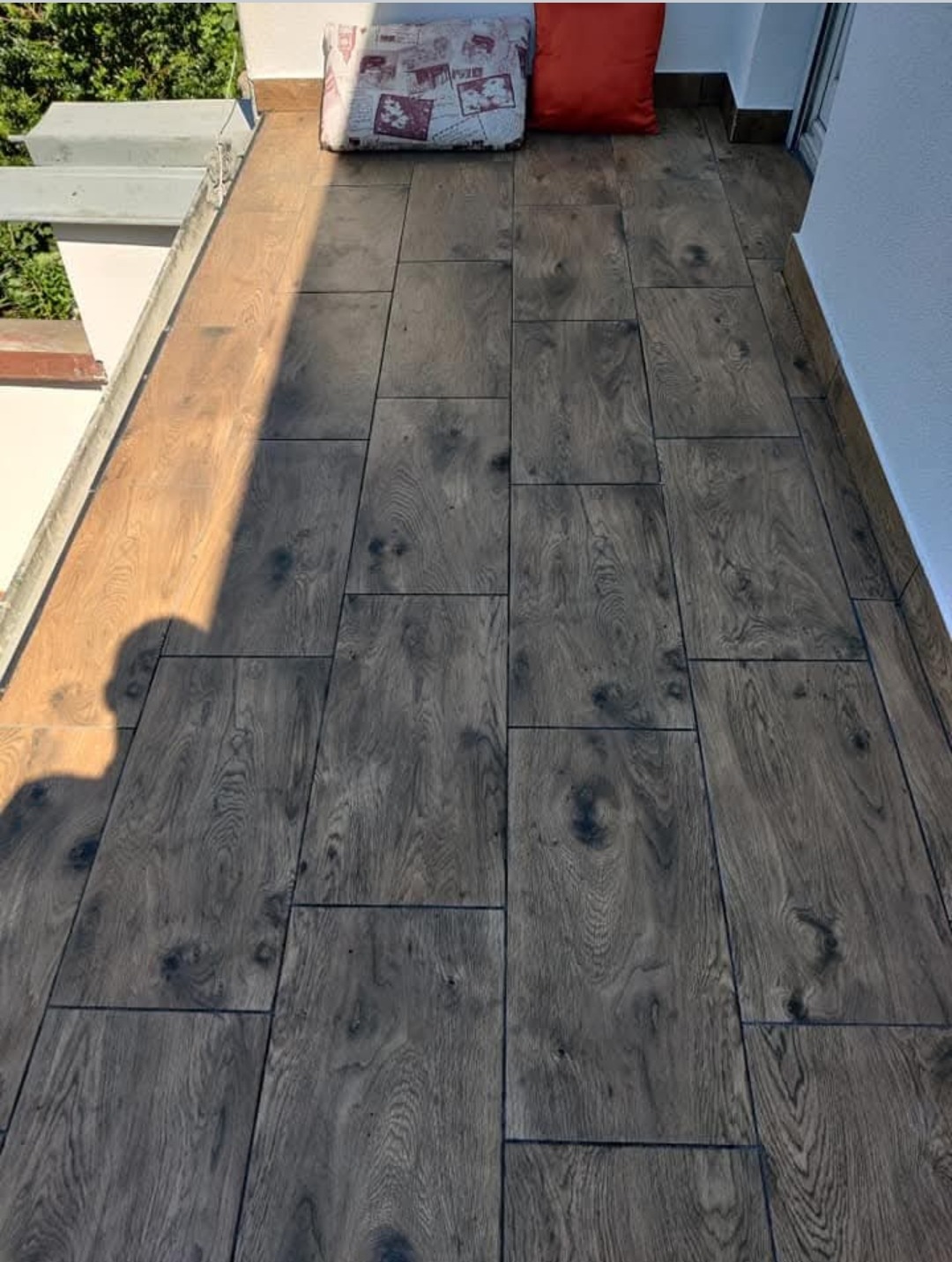 Ułożone panele podłogowe imitujące drewno na balkonie w Józefowie, widoczny cień osoby i poduszki dekoracyjne.