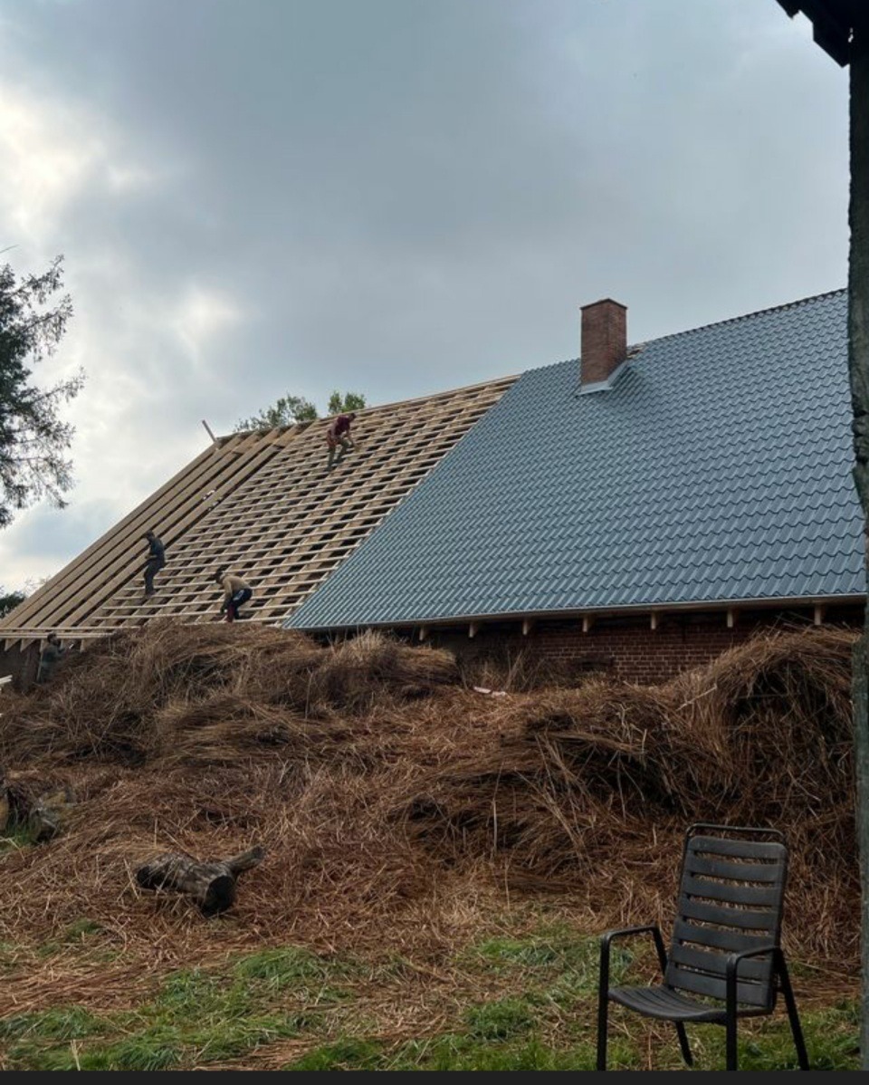 Ekipa dekarzy w Zgorzelcu pracuje nad wymianą pokrycia dachu na budynku gospodarczym; widoczny fragment nowej dachówki i odkryta więźba dachowa, na pierwszym planie sterta siana.