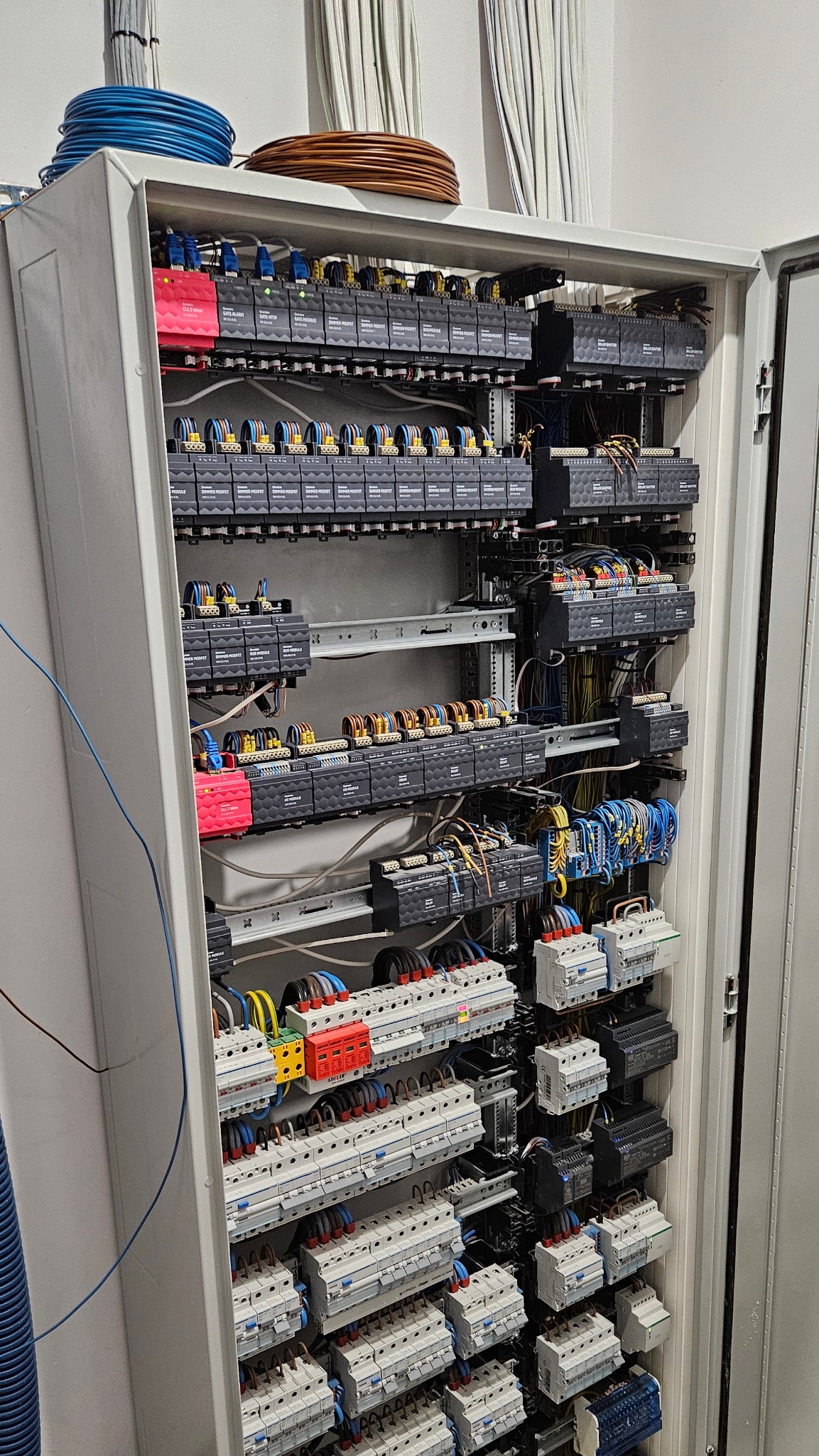 Otwarta szafa sterownicza z licznymi modułami, przewodami i zabezpieczeniami, zwoje kabli na górze szafy.