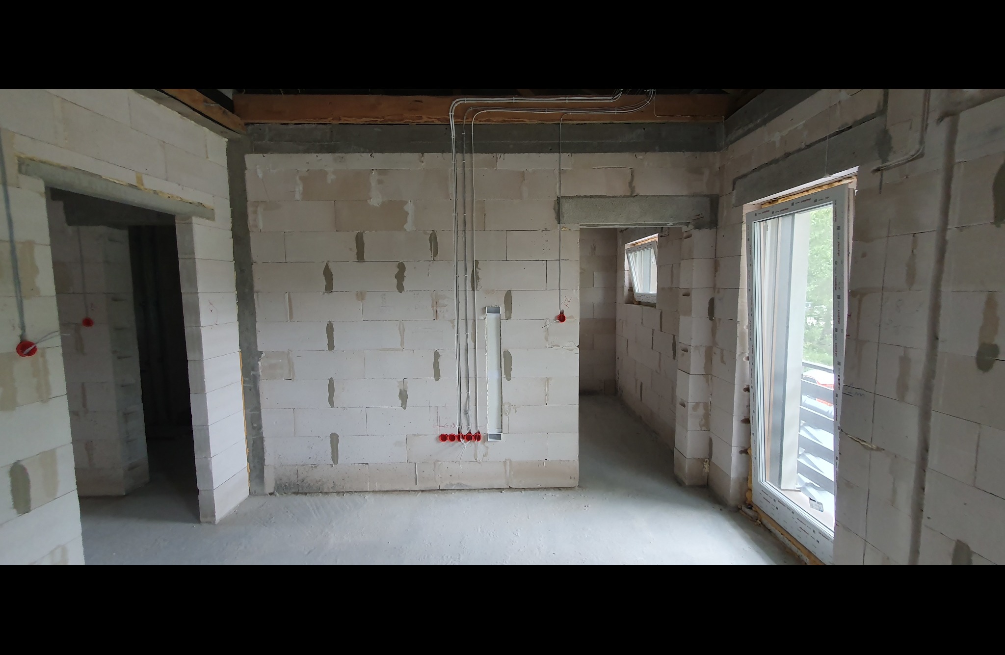 Surowy stan wnętrza z instalacją elektryczną: widoczne przewody w peszlach, puszki podtynkowe, ściany z betonu komórkowego przed wykończeniem.