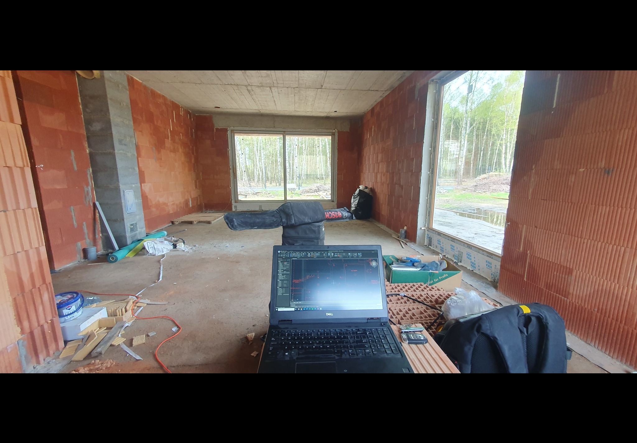 Projekt instalacji elektrycznej wyświetlony na laptopie Dell w surowym wnętrzu budynku z czerwonej cegły, widoczne narzędzia i materiały budowlane.