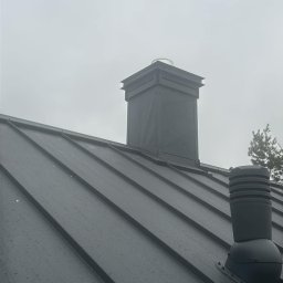 KaroDACH Dawid Sosiński - Metalowy dach z kominem i wentylacją w pochmurny dzień, widoczne krople deszczu.