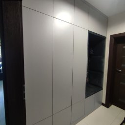 Mateusz Dębczyk - Szara szafa w przedpokoju z wnęką do siedzenia wyłożoną ciemną tapicerką, widok na drzwi wejściowe.