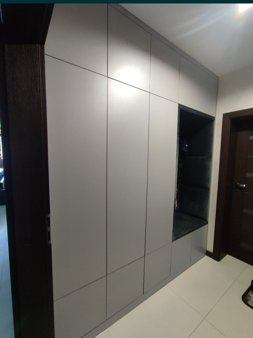 Szara szafa w przedpokoju z wnęką do siedzenia wyłożoną ciemną tapicerką, widok na drzwi wejściowe.