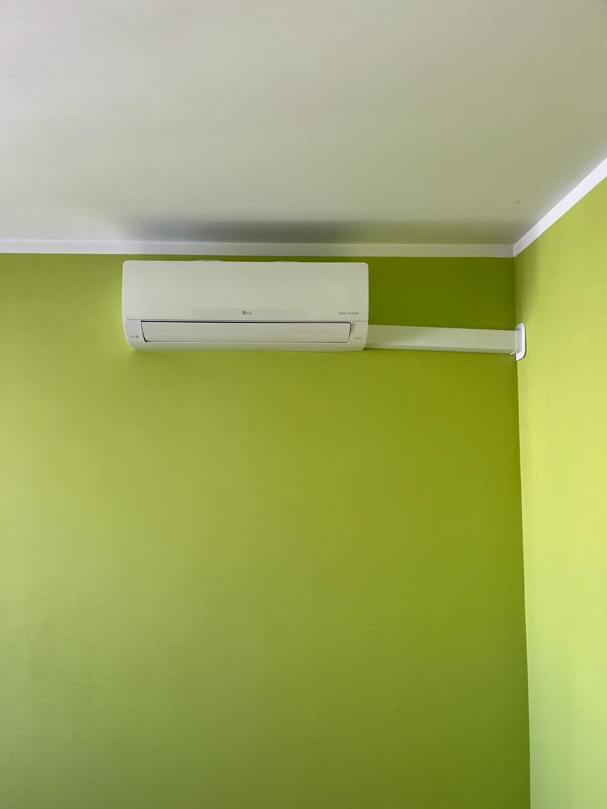 Biała klimatyzacja LG zamontowana na ścianie w odcieniu limonki, widoczna z przodu. Minimalistyczny design, białe rurki montażowe.