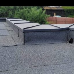 Usługi Blacharsko-Dekarskie oraz niewielkie prace ogolnobudowlane . Magdalena Zagaja - Szczegółowe ujęcie płaskiego dachu pokrytego papą, z widocznymi obróbkami blacharskimi w kolorze grafitowym. Widoczny otwór wentylacyjny w elewacji dachu.