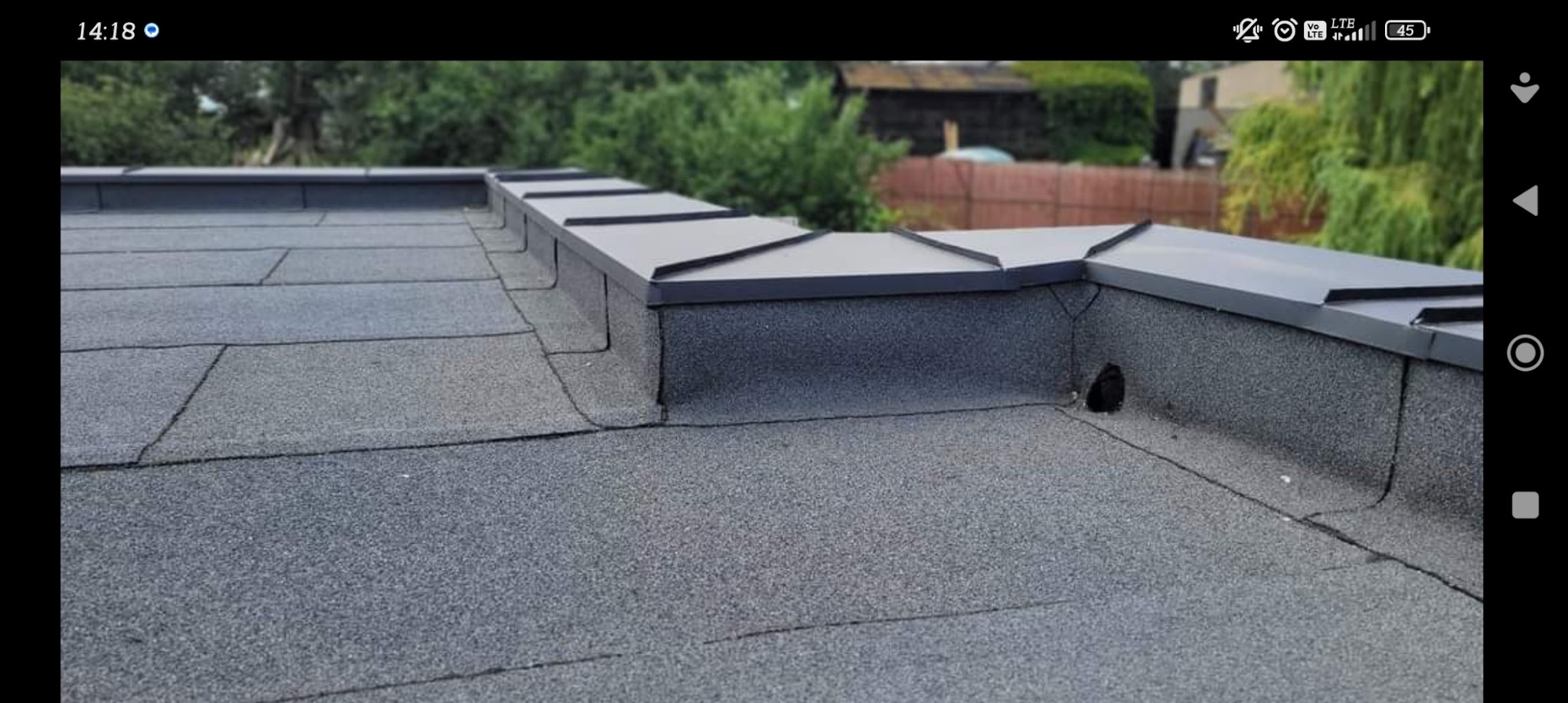 Szczegółowe ujęcie płaskiego dachu pokrytego papą, z widocznymi obróbkami blacharskimi w kolorze grafitowym. Widoczny otwór wentylacyjny w elewacji dachu.