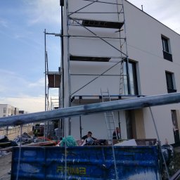 VOLODYMYR IVANOV - Nowoczesny budynek w trakcie prac wykończeniowych elewacji, widoczne rusztowania, kontener na odpady budowlane oraz pracownicy.