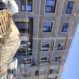 VOLODYMYR IVANOV - Budynek w trakcie ocieplania, widoczne płyty styropianowe na elewacji, rusztowania i pracownik w kombinezonie na rusztowaniu.