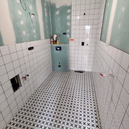 Szymon Zasępa - Łazienka w trakcie wykończenia: białe płytki na ścianach, wzorzysta podłoga, zabudowa stelaża WC. Widoczne instalacje i płyty gipsowo-kartonowe.