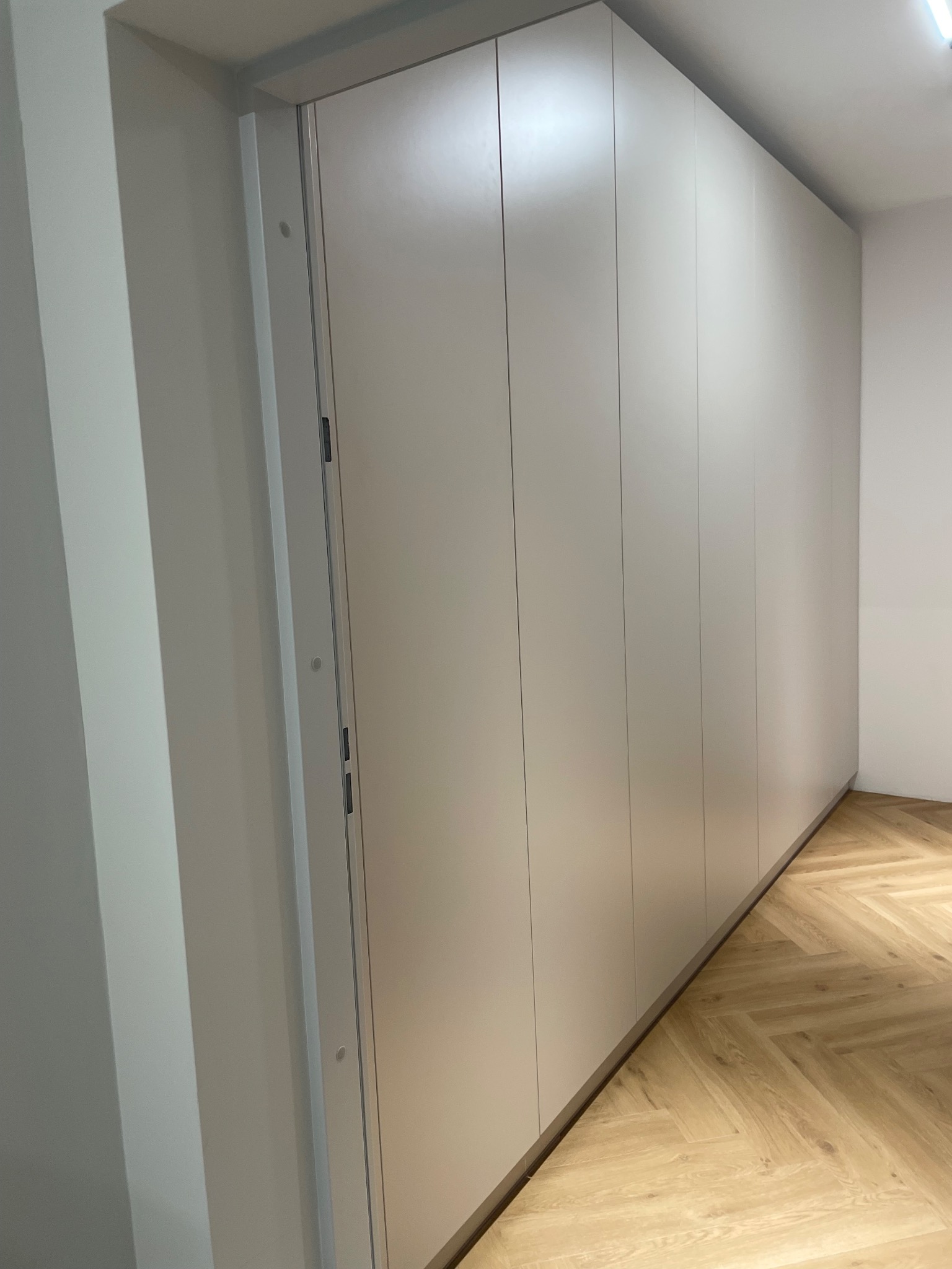 Jasna szafa wnękowa z ukrytymi uchwytami, dopasowana do podłogi w jodełkę, minimalistyczny design, widok z boku, oświetlenie naturalne.