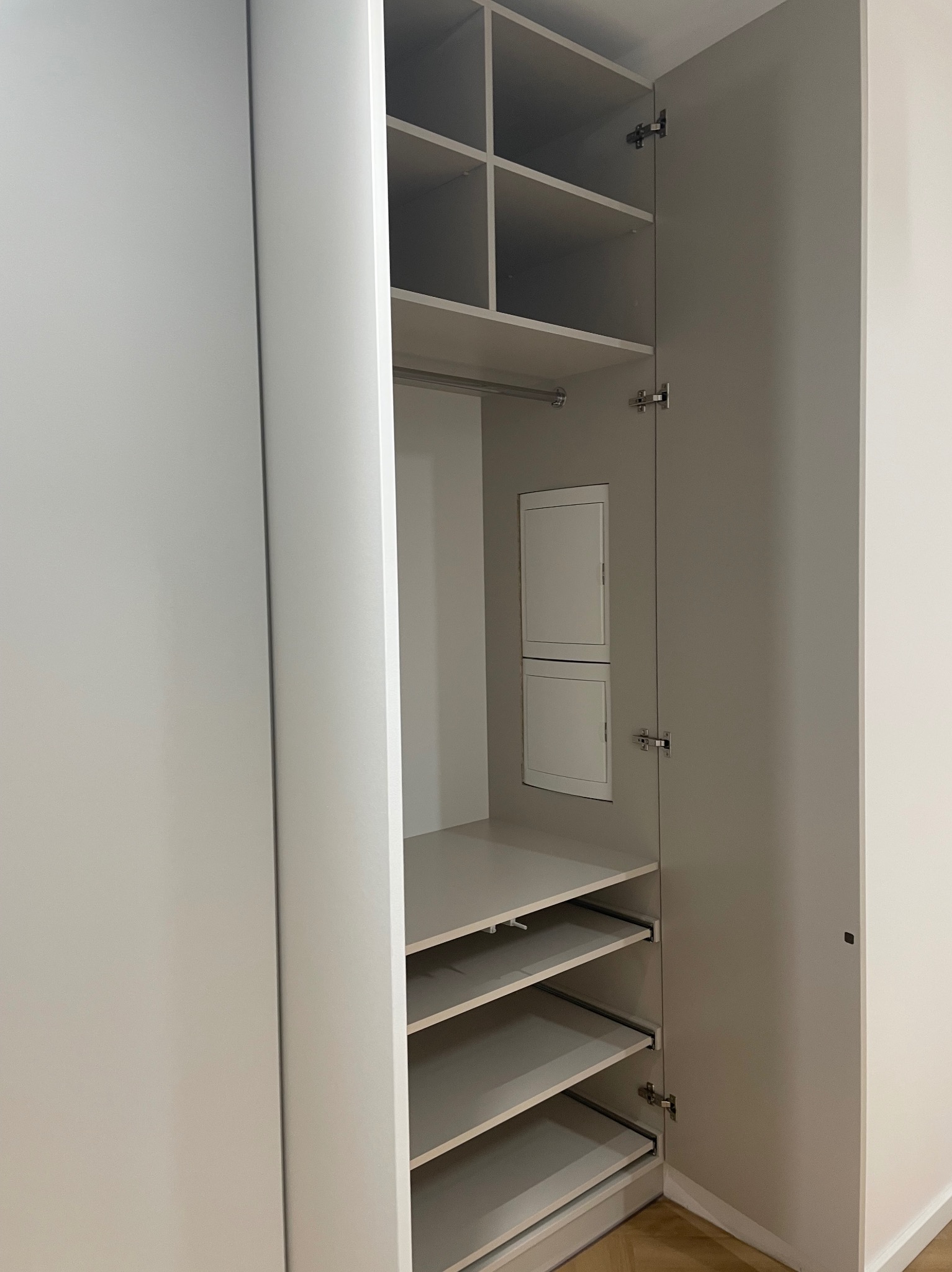 Otwarta, jasnoszara szafa wnękowa z półkami i szufladami, widok z bliska na wnętrze, minimalistyczny design, metalowe okucia, gładkie fronty.