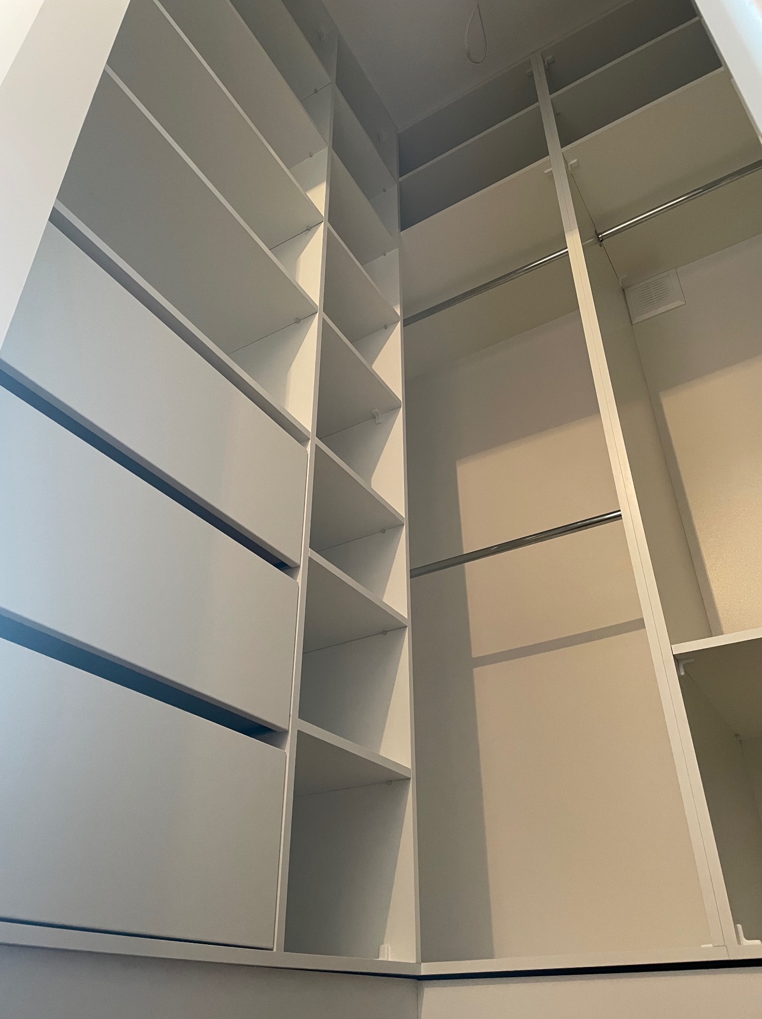 Wnętrze szafy wnękowej z białymi półkami, szufladami i drążkami, widok z dołu ukazujący przestrzeń i układ elementów.