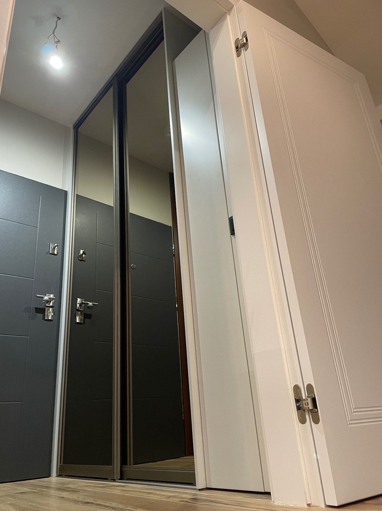 Nowoczesna szafa wnękowa z lustrzanymi drzwiami przesuwnymi, widoczna obok biała ściana z drzwiami. Ujęcie z dołu, ukazujące montaż i wykończenie.