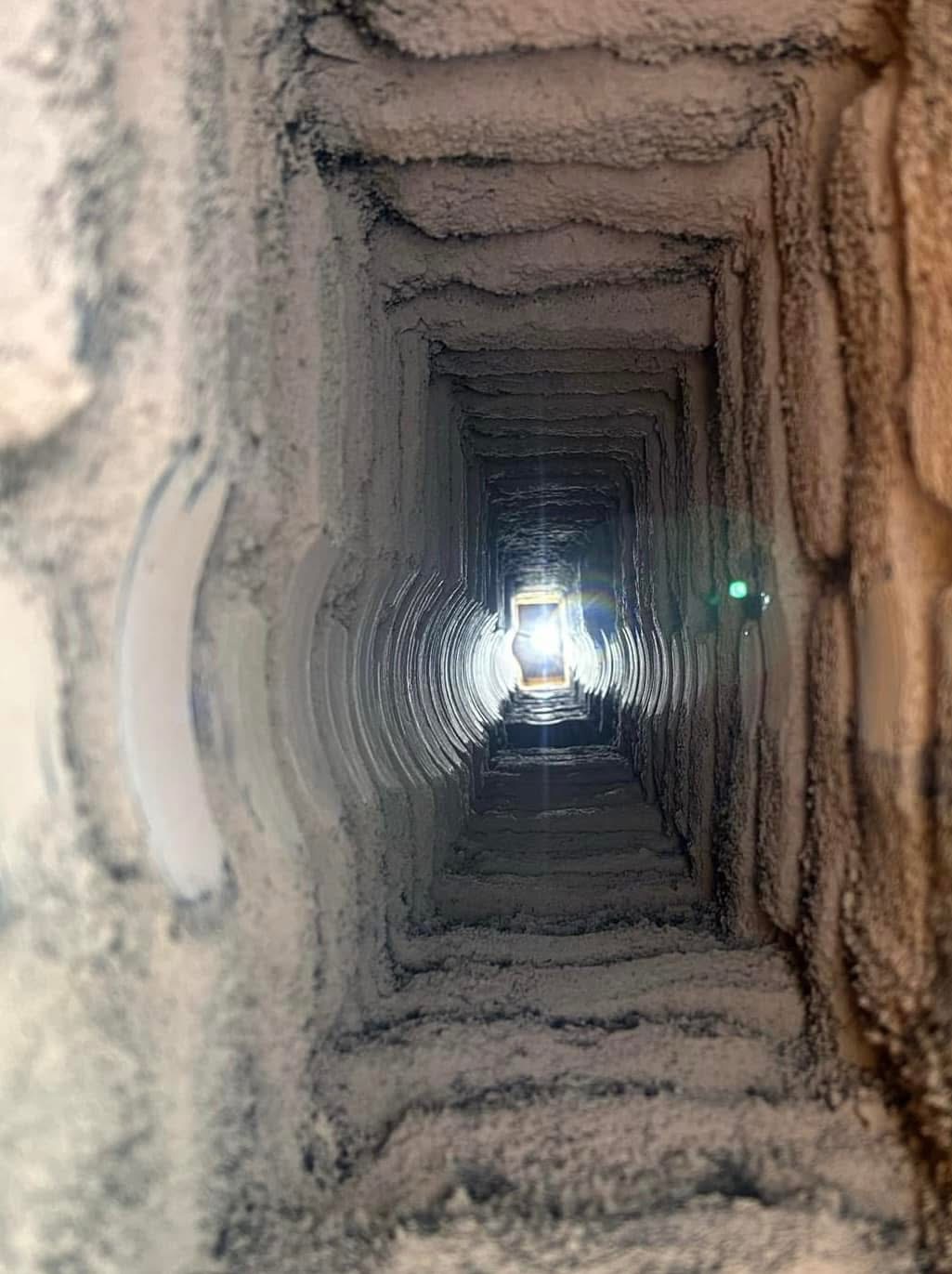 Wnętrze kanału wentylacyjnego lub komina, silnie zabrudzone sadzą i pyłem, oświetlone odległym źródłem światła.