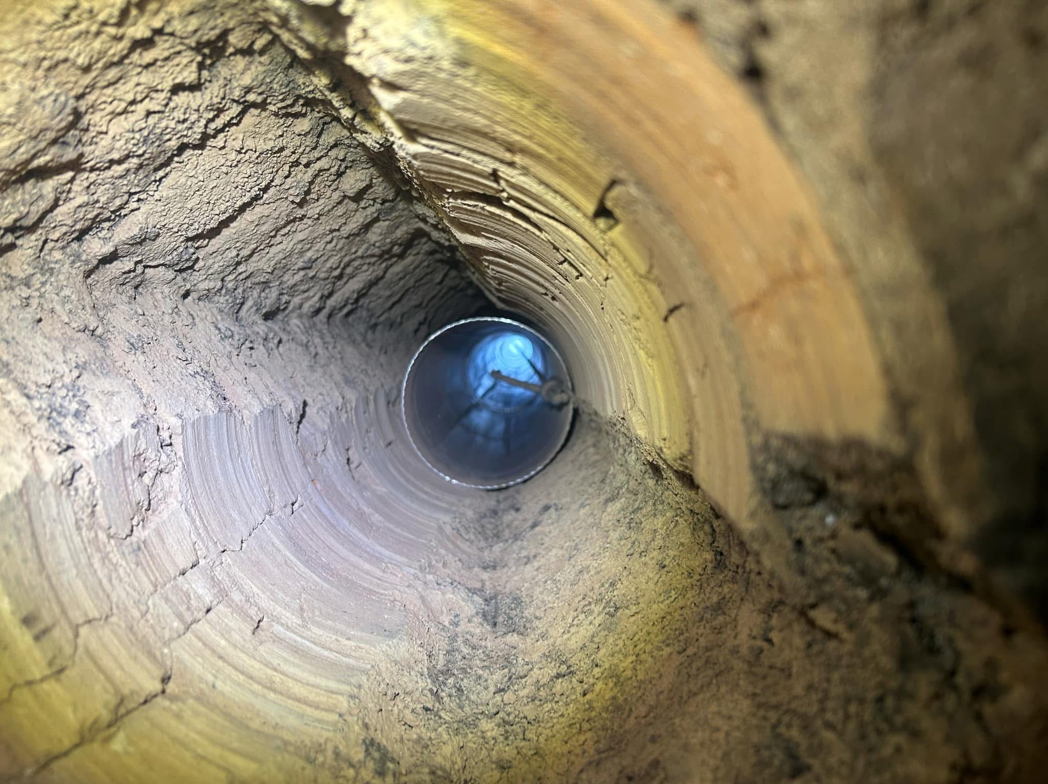 Wnętrze komina z widoczną stalową rurą wkładu kominowego, oświetlone od dołu, z osadami sadzy na ścianach.