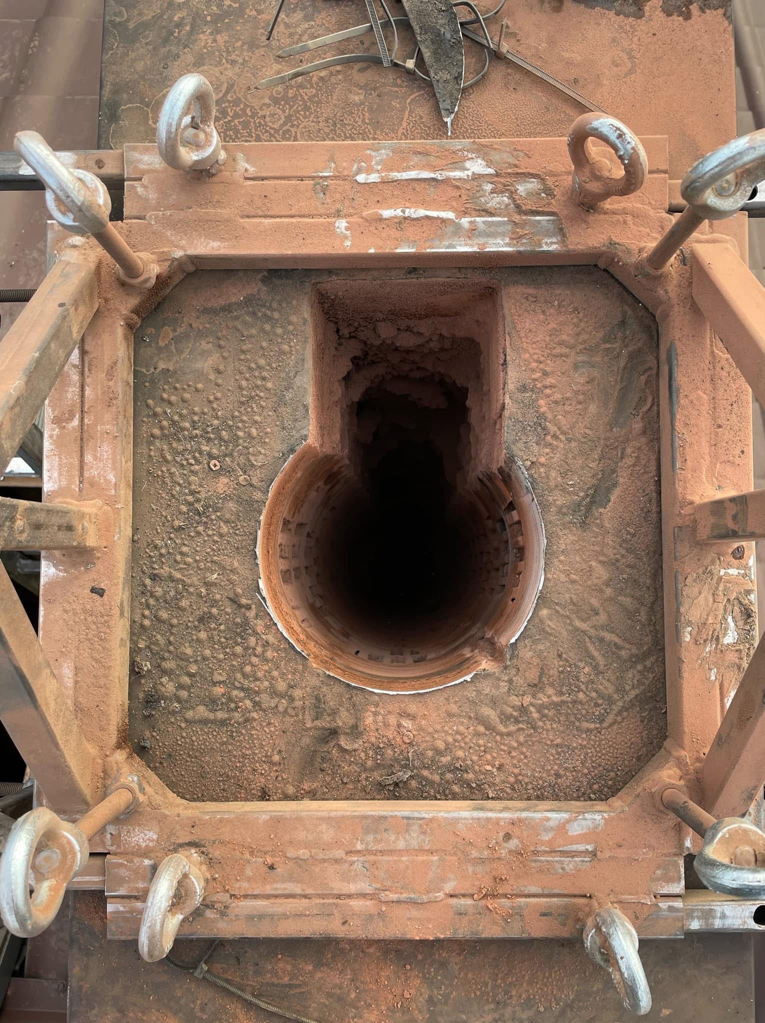 Wnętrze komina z widoczną konstrukcją wsporczą i metalowymi uchwytami, pokryte warstwą pyłu i zabrudzeń.