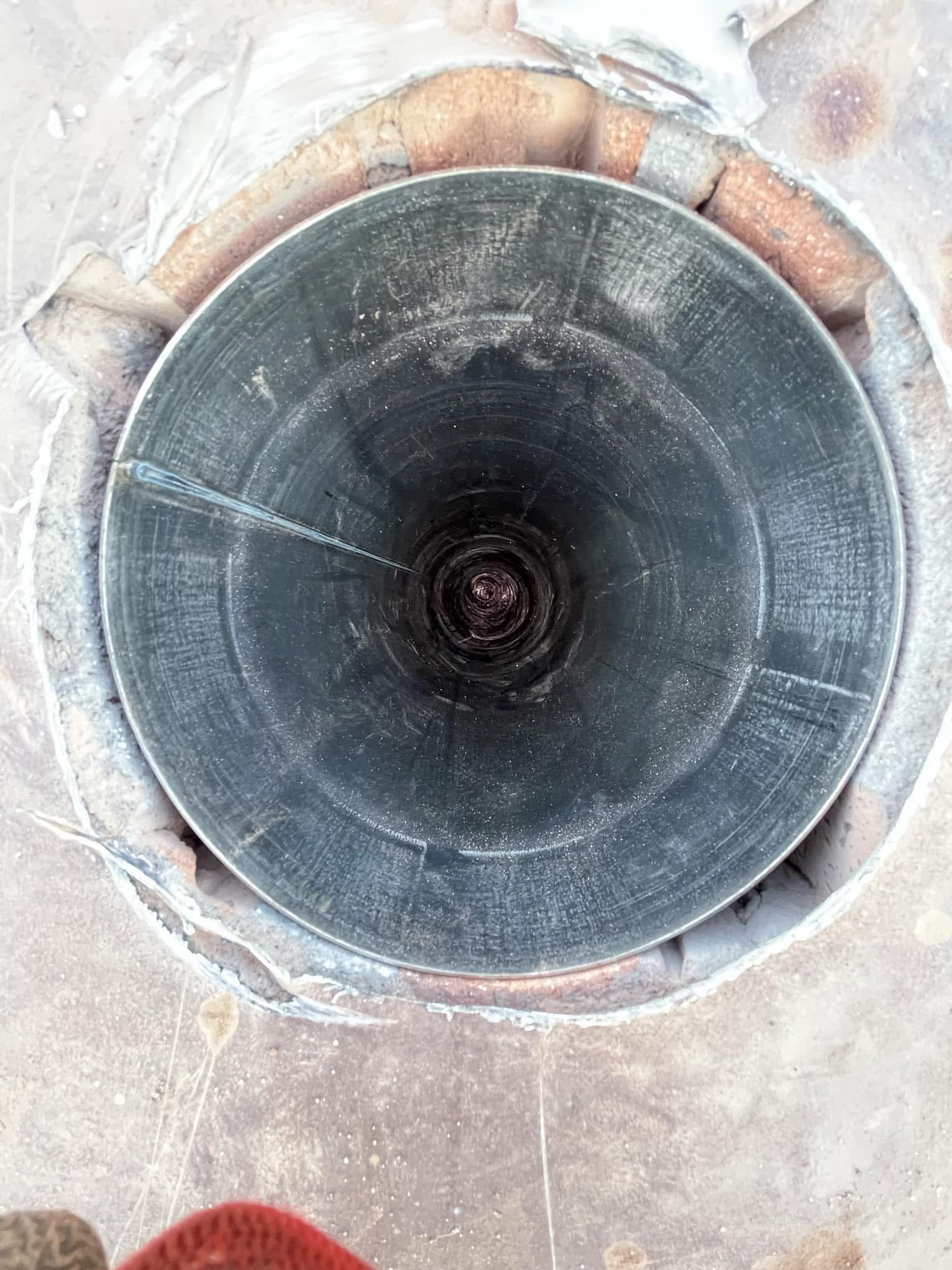 Wnętrze metalowego przewodu kominowego widziane z góry, z widocznymi śladami spawania i zabrudzeniami, otoczone ceglaną konstrukcją z zaprawą.