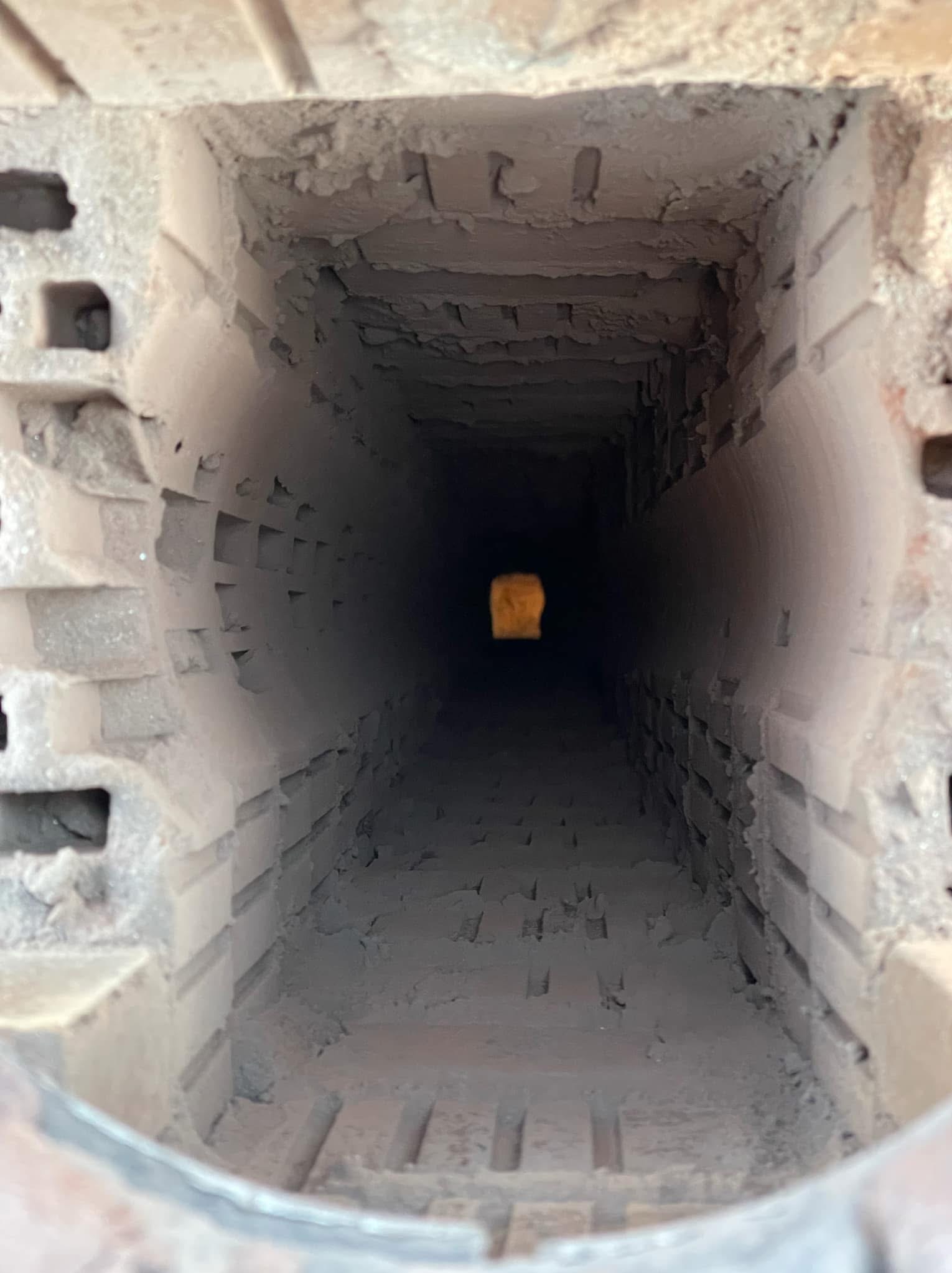 Wnętrze ceglanego przewodu kominowego widziane od dołu, z widocznym światłem na końcu tunelu.