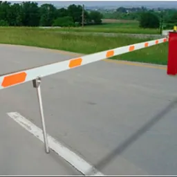 Szlaban parkingowy z pomarańczowymi elementami odblaskowymi, widok z boku na tle zieleni.