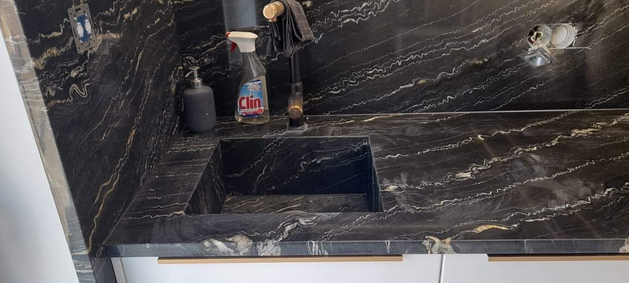 Czarny, wzorzysty blat kamienny z wbudowanym zlewem w Smardzowie, z widocznym dozownikiem mydła i płynem do czyszczenia.